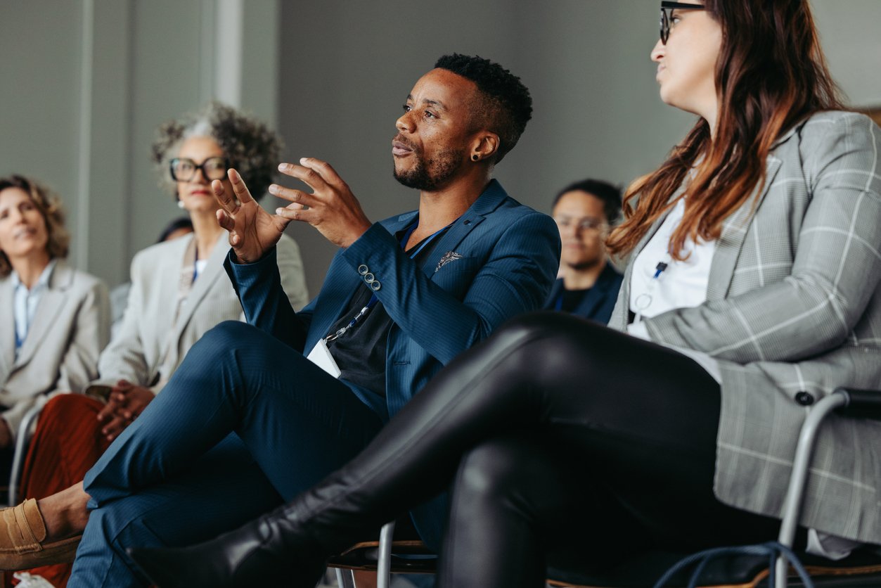 A group of professionals seated in a conference setting. One person is speaking.