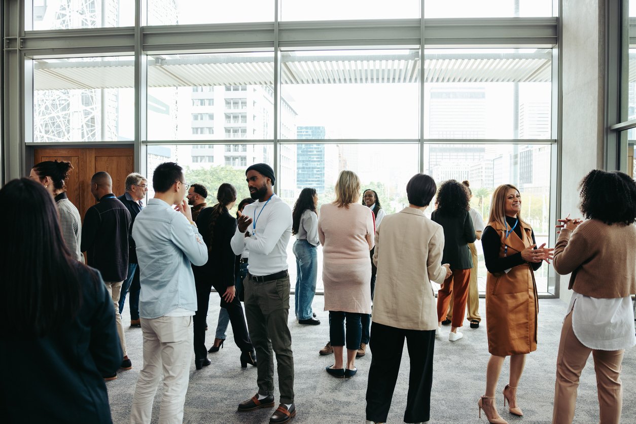 A group of professionals mingling in a bright, open room in a building. A group of professionals mingling in a bright, open room in a building.